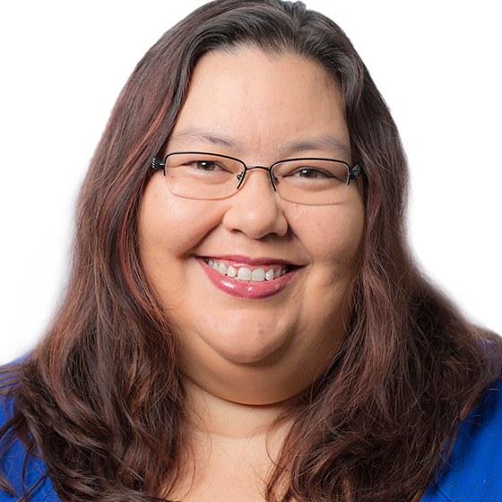 Smiling woman with mid-length brown hair wearing glasses and a blue top, against a solid white background.